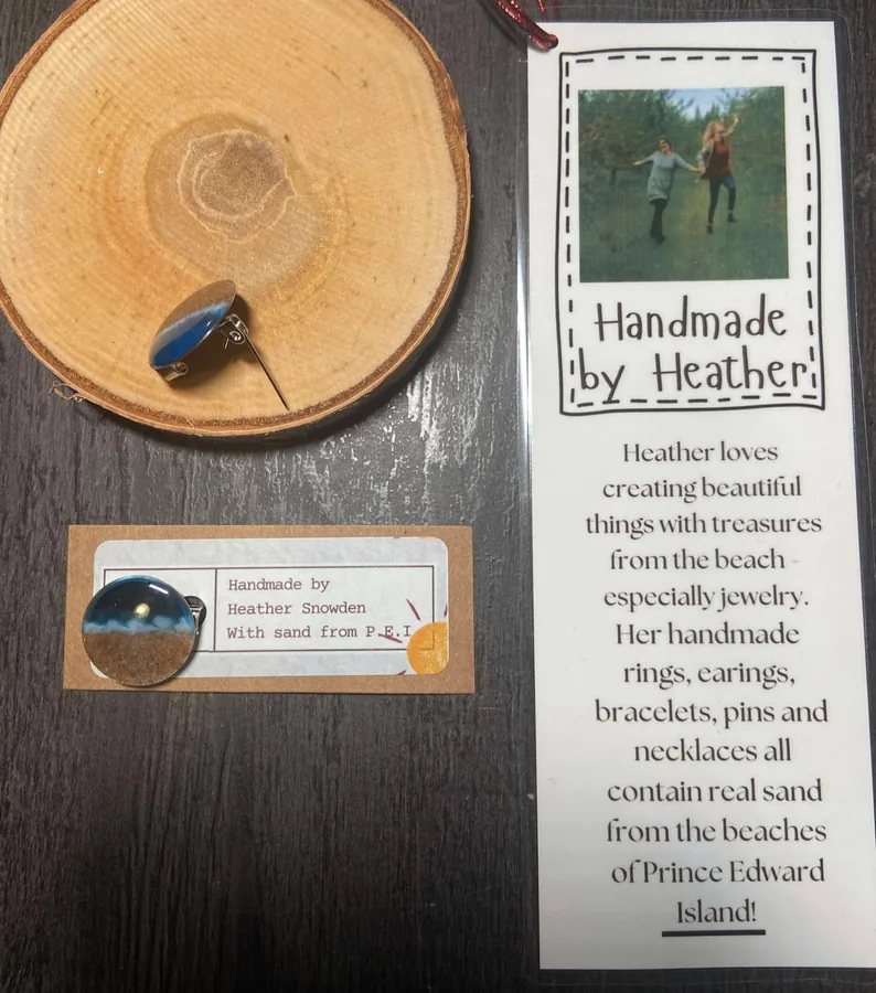 A lapel pin made of PEI sand on a wood slice, with the Handmade by Heather maker card