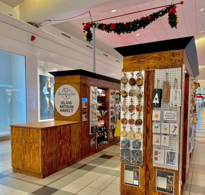 The wooden Branching Out kiosk inside Royalty Crossing Mall, shelves of makers&rsquo; goods and Christmas garland